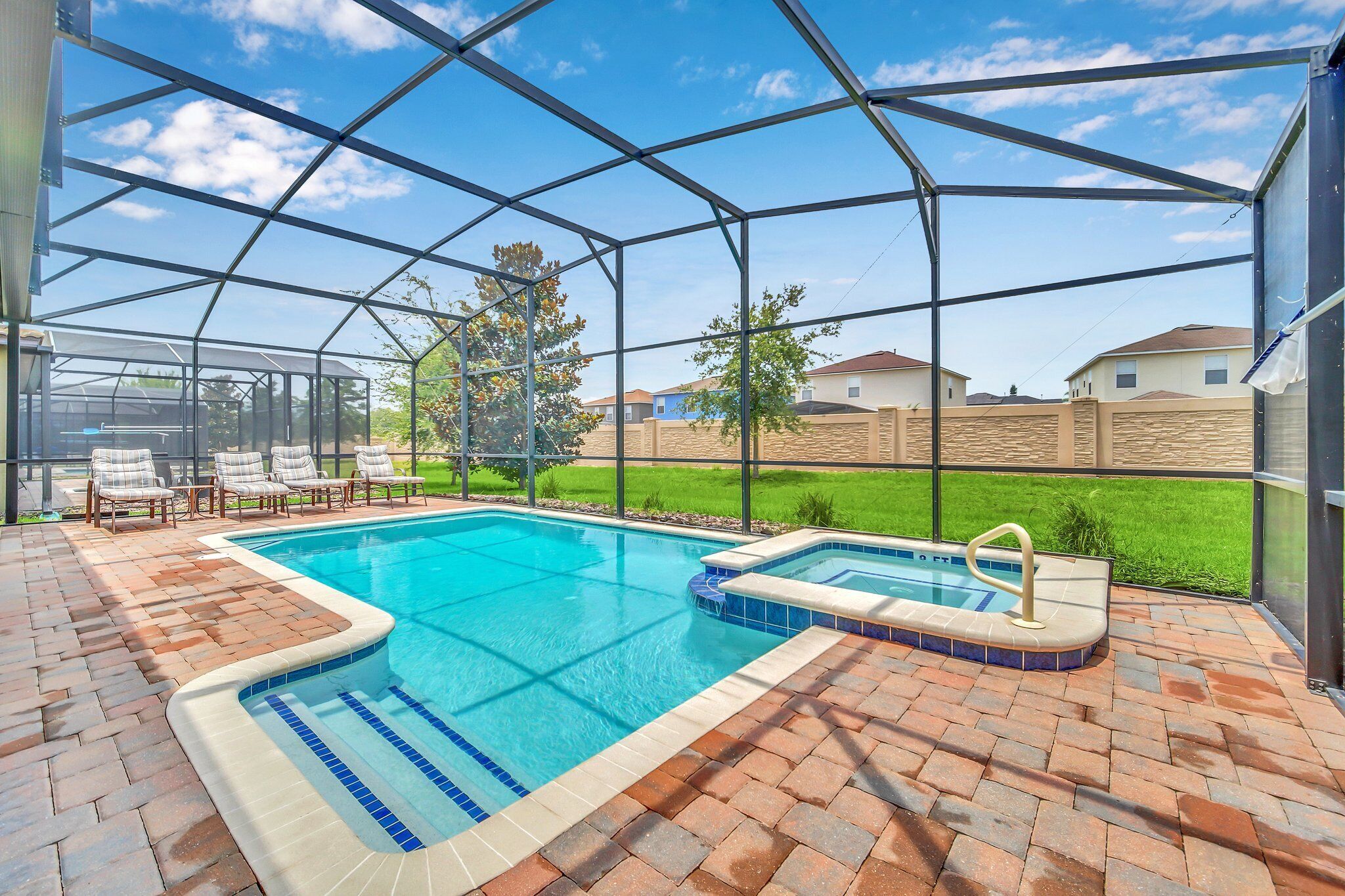 A covered outdoor swimming pool with a patio area, a hot tub, and a view of a residential neighborhood.