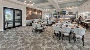 A spacious dining area with multiple tables and chairs, a large kitchen in the background, and a patterned carpet. - Water Park included. Spa & Golf Resort Near Disney! (Champions Gate)