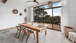 Een moderne eetruimte met een houten tafel, geweven stoelen en een grote schuifdeur naar een terras.