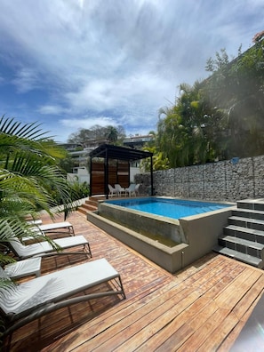 A swimming pool with a wooden deck, lounge chairs, and a stone wall.