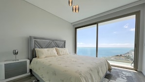 Ein Schlafzimmer mit einem großen Bett, einem Nachttisch und Meerblick durch ein großes Fenster.