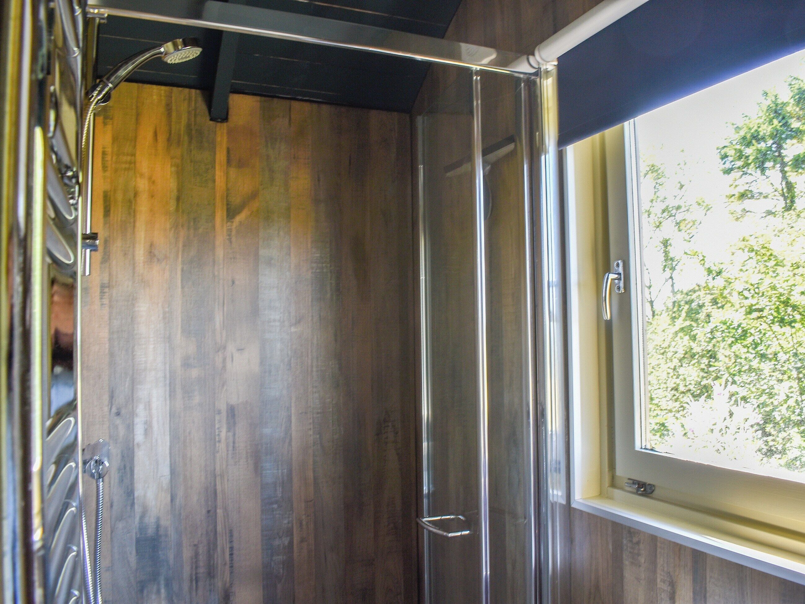 A shower with a wooden wall and a window.