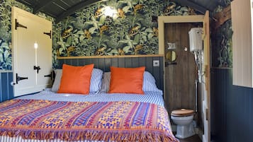 A bedroom with a bed, two orange pillows, a patterned blanket, a wooden headboard, a wall with a monkey mural, and a wooden door.