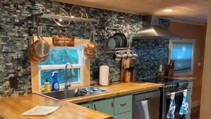 A kitchen with a wooden countertop, a stone backsplash, hanging pots, a stove, and a window. - 2BR/2BA, Clean, Comfy & Steps from Dining & Sound w/ Tesla charging station  (Emerald Isle)