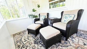 A room with wicker furniture, including two chairs and a small table, with a patterned rug on the floor.