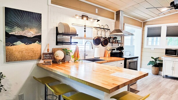 A modern kitchen with a wooden island, bar stools, hanging pots, and a globe on the counter. - Boho, plant-filled home w/ wood + leather touches, 3 beds, 2 baths, super clean. (Emerald Isle)
