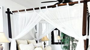 A four-poster canopy bed with a wooden frame, white bedding, and a white canopy. - Boho, plant-filled home w/ wood + leather touches, 3 beds, 2 baths, super clean. (Emerald Isle)
