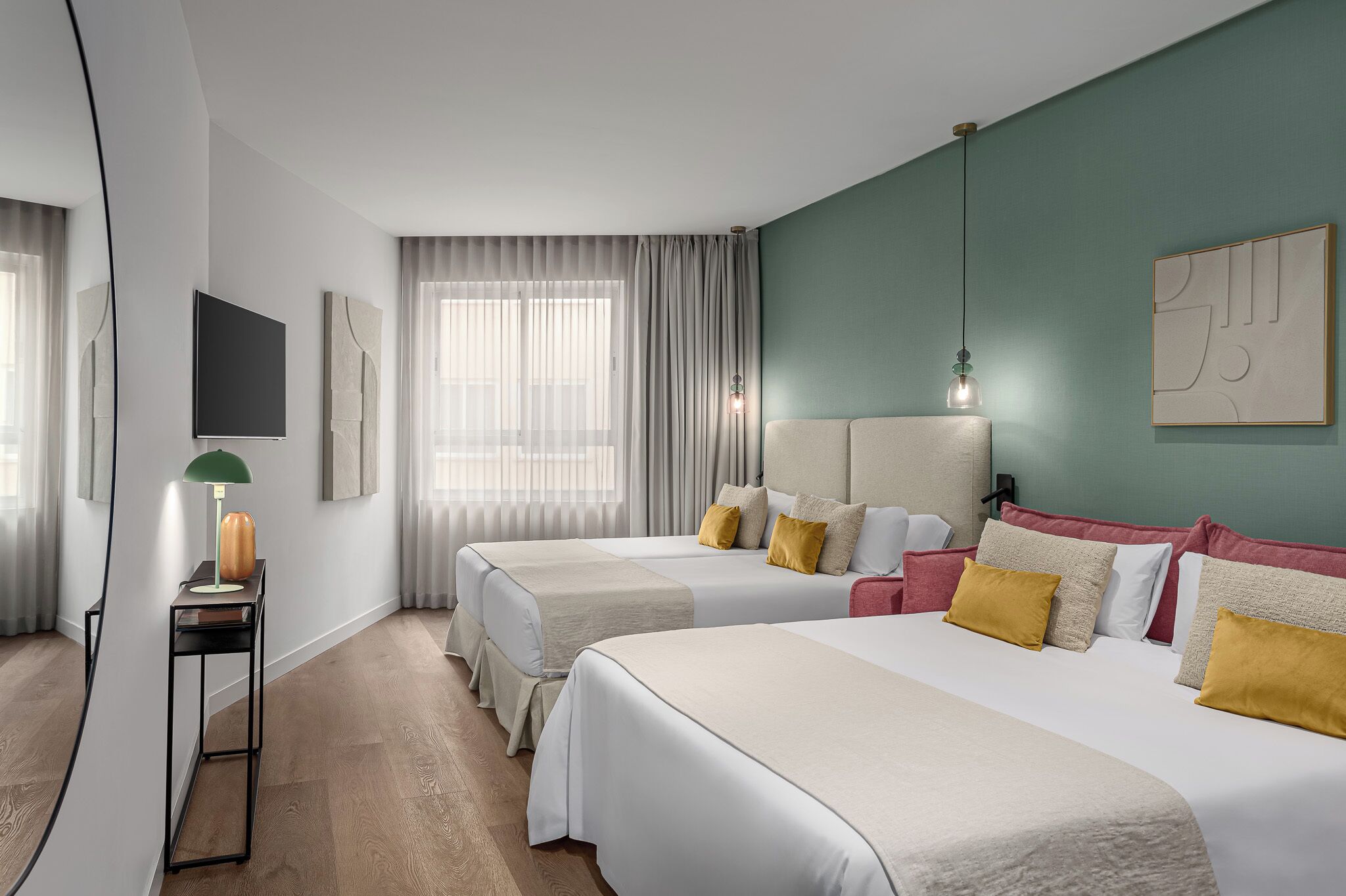 A hotel room with two beds, a desk, a lamp, and a TV.