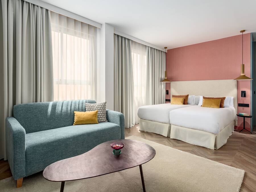 Ett modernt hotellrum med en blå soffa, en vit säng och ett litet bord med en skål på.