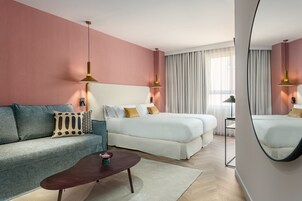 A modern hotel room with a large bed, a sofa, a coffee table, and a mirror.