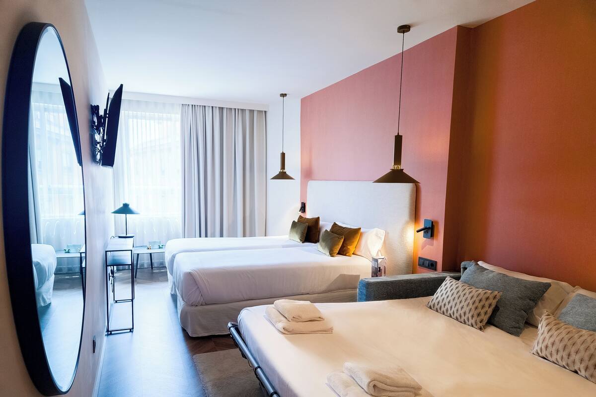 Une chambre d’hôtel avec deux lits, un grand miroir, un bureau avec une chaise et une fenêtre avec des rideaux.