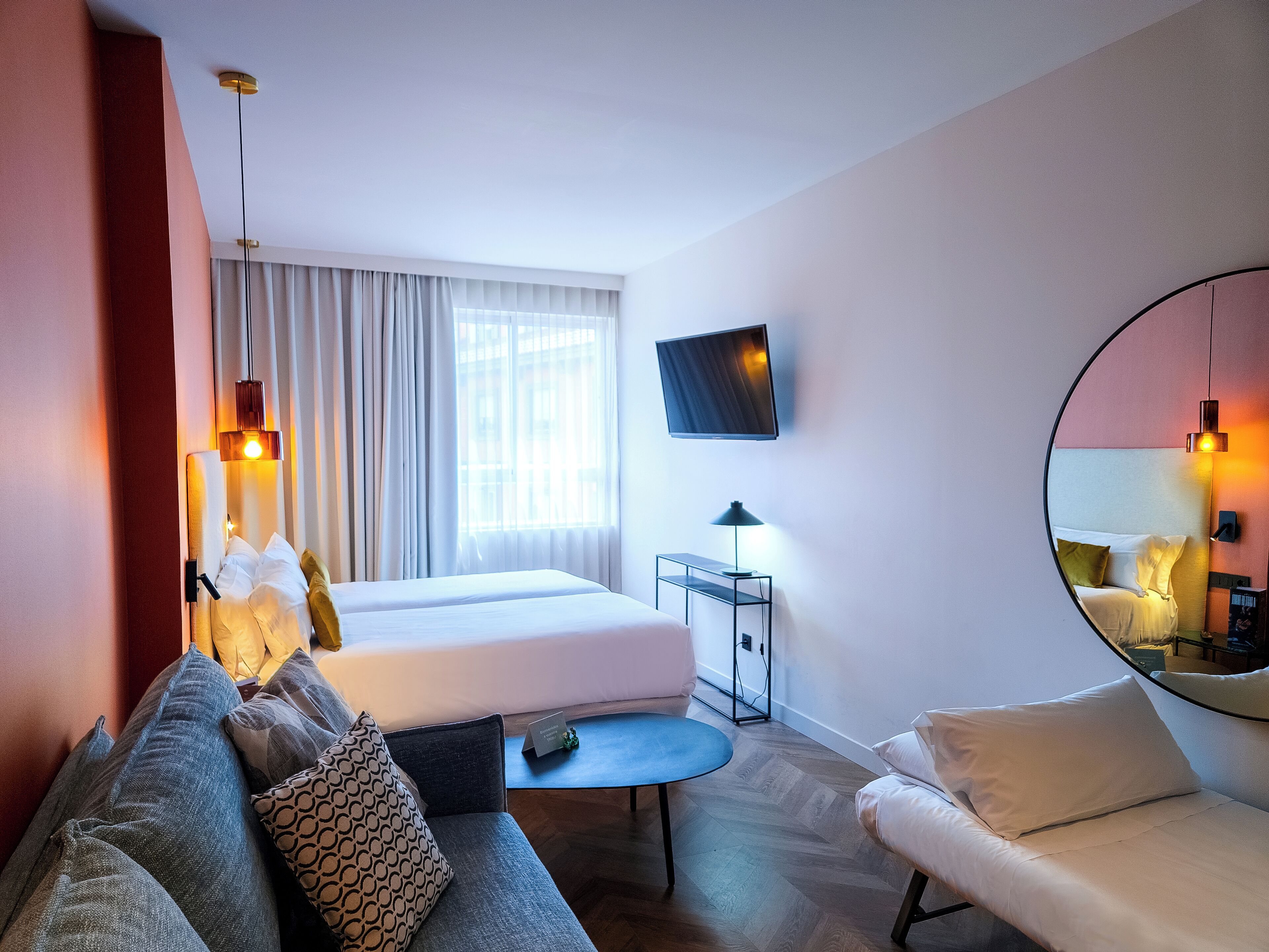 Habitación de hotel con cama, sofá, una mesita, televisor y espejo.