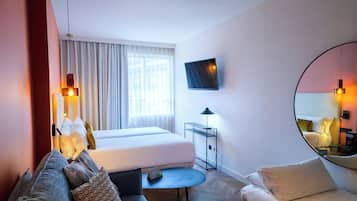 Habitación de hotel con cama, sofá, una mesita, televisor y espejo.