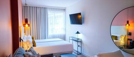 A hotel room with a bed, a sofa, a small table, a TV, and a mirror.