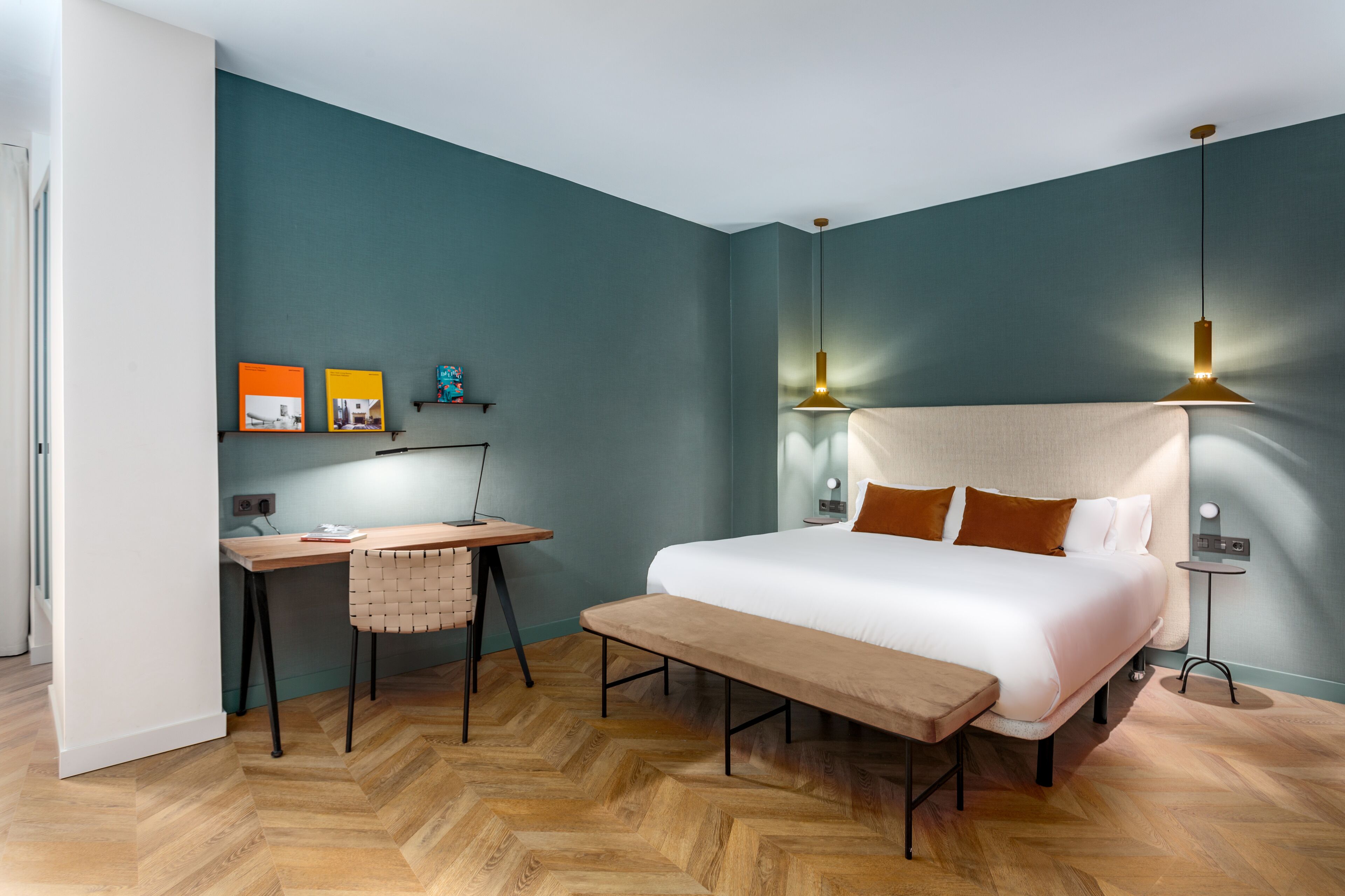 A bedroom with a bed, bedside table, lamp, and a desk with a chair.