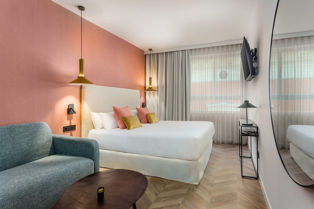 Une chambre d’hôtel comprenant un lit, un canapé, une table basse, un téléviseur fixé au mur et une fenêtre avec des rideaux.
