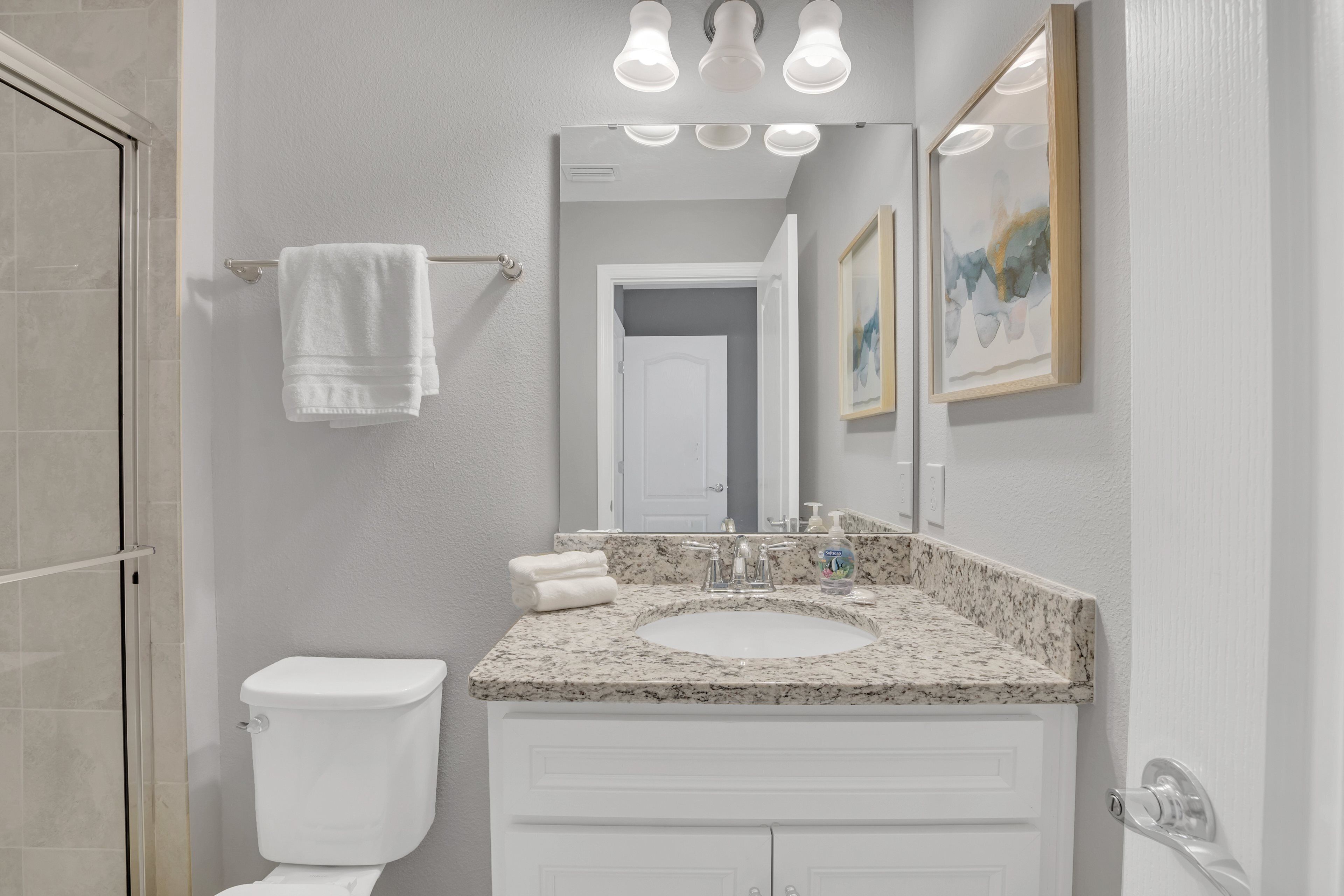 Une salle de bain avec des toilettes blanches, un lavabo doté d’un plan de travail en marbre et un miroir au-dessus du lavabo.