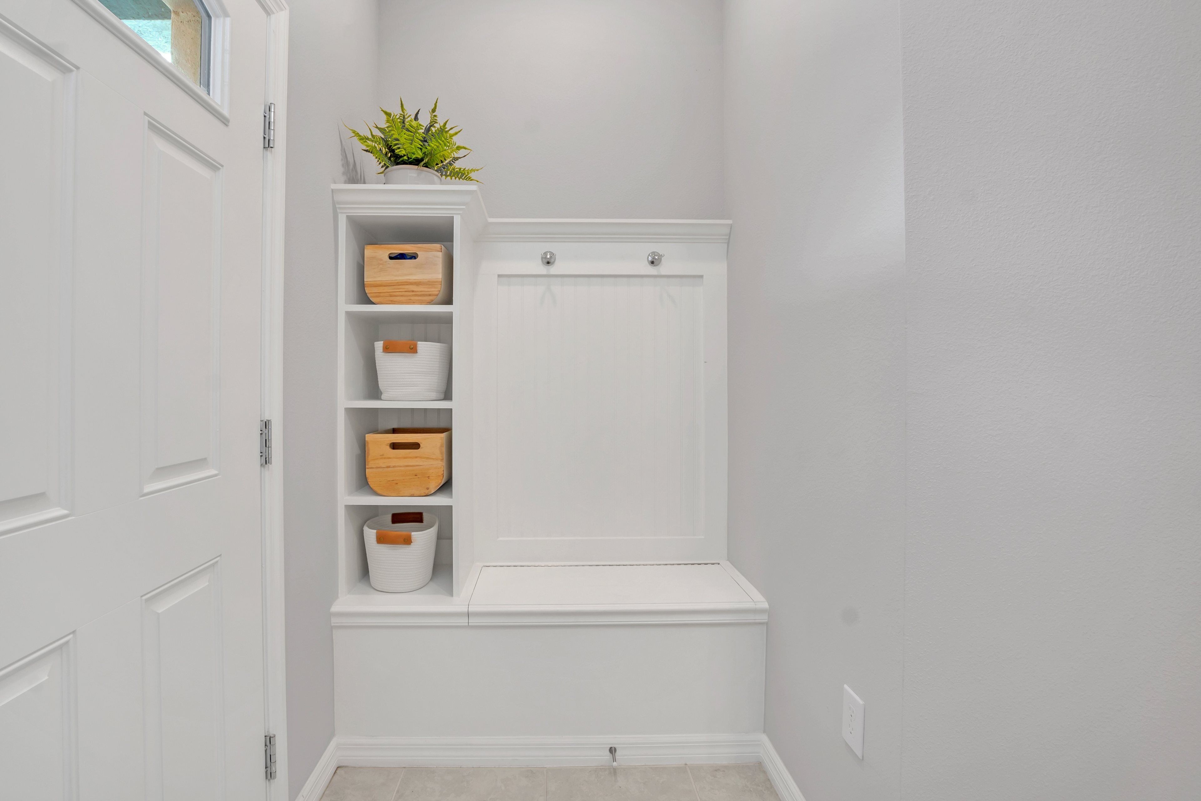 Un couloir aux murs blancs, avec un banc intégré doté de tiroirs de rangement et une plante en pot posée sur le dessus.