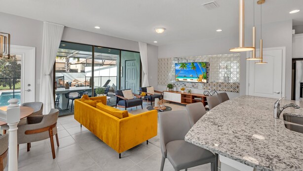 A modern living room with a yellow sofa, a dining area, a kitchen with a granite countertop, and a large TV on the wall. - Headline (Kissimmee)