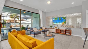 A modern living room with a yellow sofa, a TV on the wall, and a balcony with a view of palm trees. - Headline (Kissimmee)