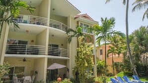 Un hotel de varios pisos con balcones, mobiliario exterior y palmeras.