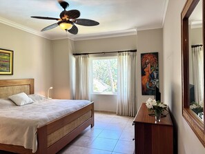 A bedroom with a bed, a ceiling fan, a window with curtains, a painting, and a mirror. - Elegant 2-bedroom apartment in Ocean Dream (Cabarete)