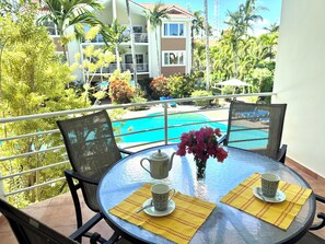 A round table with two chairs, a vase with pink flowers, a teapot, and two cups with saucers on yellow placemats. - Elegant 2-bedroom apartment in Ocean Dream (Cabarete)