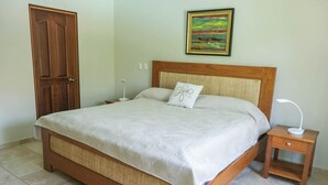 Una cama bien hecha con cabecera de madera, una mesita de noche con lámpara y un cuadro en la pared.