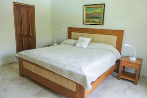 A neatly made bed with a wooden headboard, a bedside table with a lamp, and a painting on the wall.
