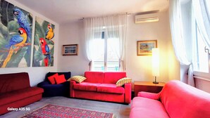 Sala de estar com sofás vermelhos, um tapete estampado e uma pintura grande de papagaios.