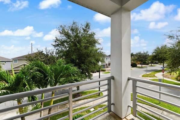 A balcony with a view of a residential street, palm trees, and houses.