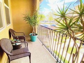 Relax on the balcony with a pair of wicker chairs and a small table, surrounded by a lush potted plant.