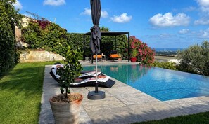 Piscina com espreguiçadeiras e um pérgola, cercada por vegetação e céu claro.