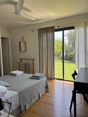 Ein Schlafzimmer mit einem Bett, einem Schreibtisch und Blick auf einen Garten durch eine Schiebetür.