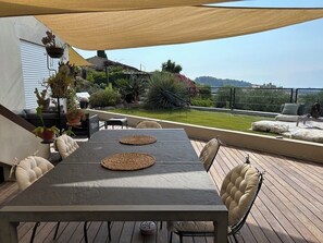 Eine Terrasse im Freien mit Tisch und Stühlen, umgeben von Topfpflanzen und Blick auf die Landschaft.