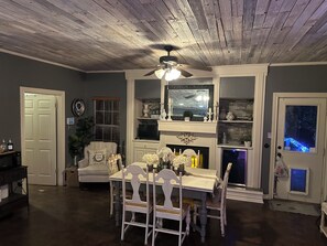 Cozy living room with a dining table for four, fireplace, and ceiling fan.