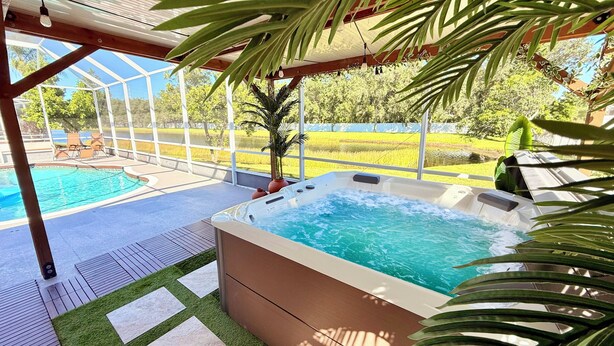 Een hottub en zwembadgedeelte met glazen dak, omgeven door groen en uitzicht op een veld.