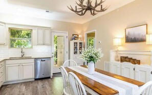 A kitchen with white cabinets, a wooden dining table, and a chandelier.