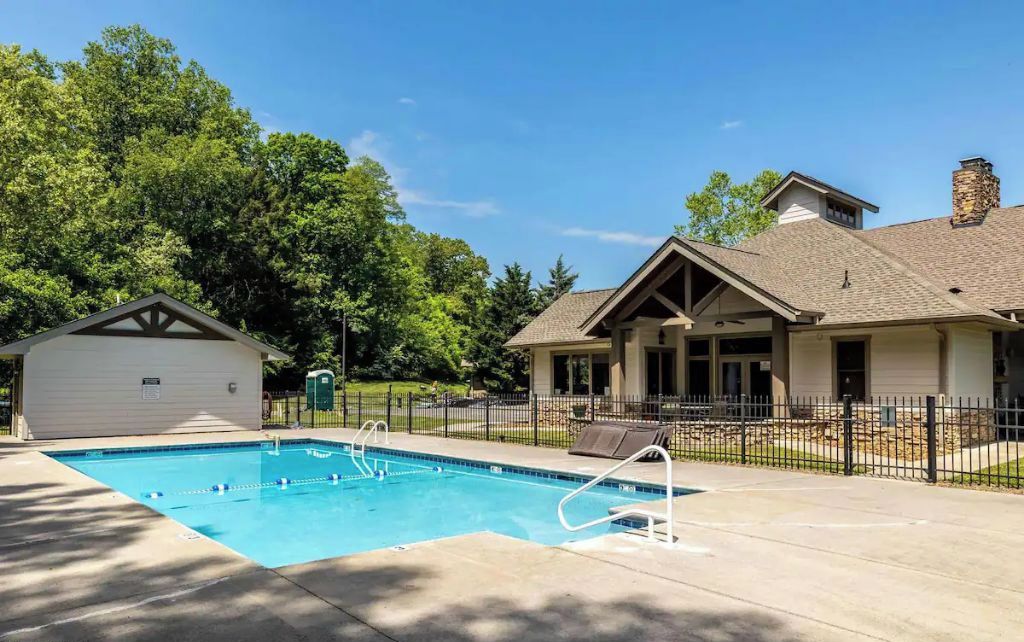 Une piscine entourée d’une clôture, un patio couvert et un bâtiment doté d’une cheminée en pierre.
