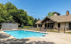 A swimming pool with a fenced area, a covered patio, and a building with a stone chimney.