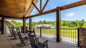 A covered outdoor seating area with wooden rocking chairs, stone pillars, and a view of a green landscape.