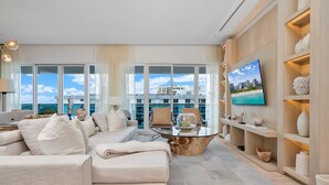 A modern living room with a large window, a flat-screen TV, and a wooden coffee table. - Premium 3-Bedroom Oceanview Penthouse at 1 Hotel (Miami Beach)