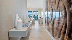 A modern hotel lobby with a long reception desk, a large abstract wall art, and a view of the city through large windows. - Premium 3-Bedroom Oceanview Penthouse at 1 Hotel (Miami Beach)
