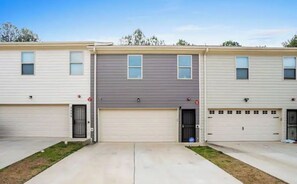 Une rangée de maisons de ville à deux étages, dotées de garages attenants, d’une allée centrale et d’un petit jardin avant.