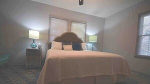 Un dormitorio con una cama grande, dos lámparas de noche, una mesita de noche y una ventana con persianas.