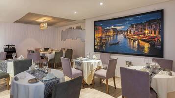 Un comedor con varias mesas dispuestas para comensales, que presenta un gran cuadro de un paisaje urbano en la pared.
