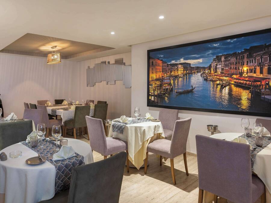Un'area pranzo con diversi tavoli apparecchiati per gli ospiti, con un'ampia pittura che raffigura un panorama urbano sulla parete.