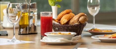 Desayuno con pan, un vaso de jugo y una botella de aceite de oliva sobre una mesa.