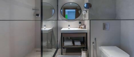 Une salle de bain moderne avec une douche à parois de verre, un lavabo avec un miroir au-dessus, des toilettes et une petite étagère avec des serviettes.