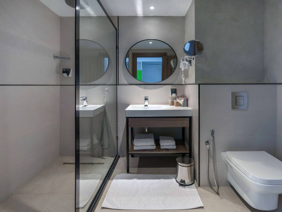 Un baño moderno con cabina de ducha de vidrio, un lavamanos con espejo, inodoro y un estante pequeño con toallas.